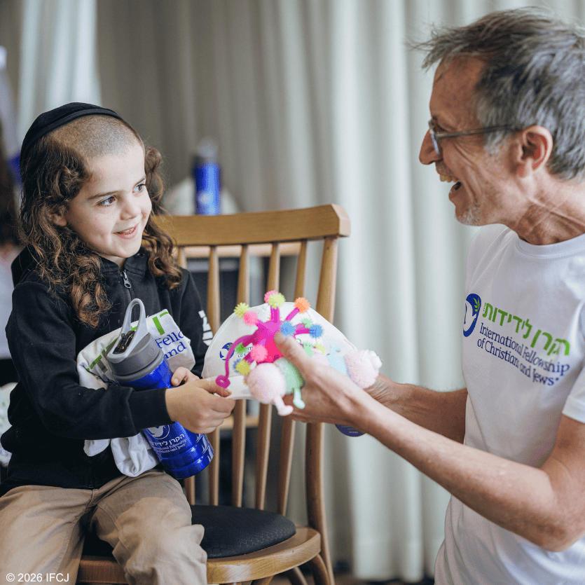 A young girl and an older man share a joyful moment during a celebration, with the girl holding a colorful cake and the man smiling warmly.