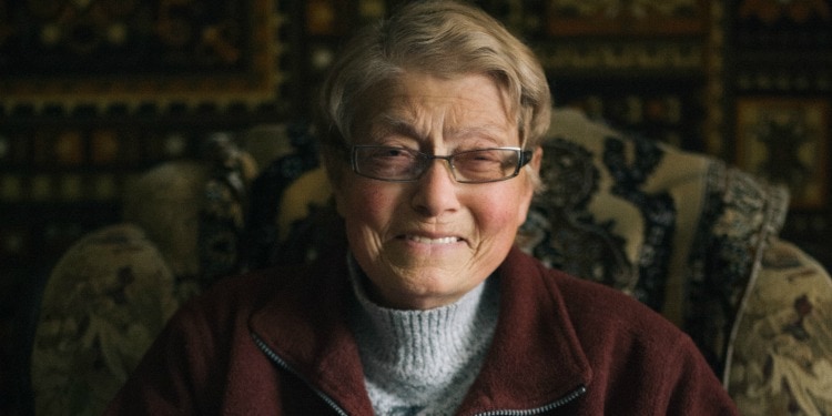Esfir, an IFCJ recipient smiling directly at the camera while sitting in a patterned chair.