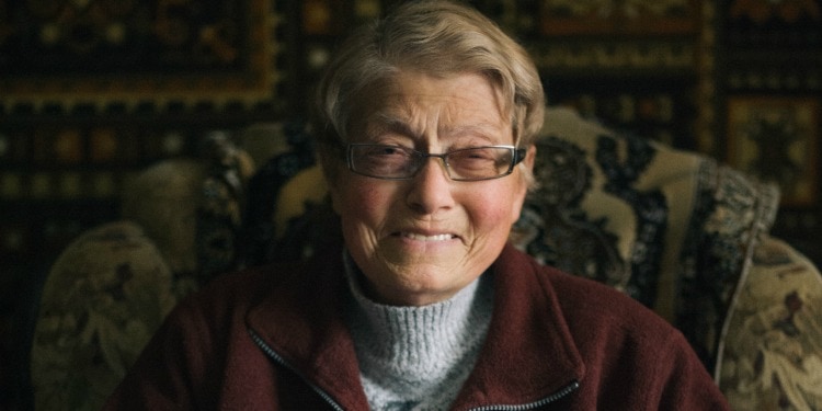 Esfir, an IFCJ recipient smiling directly at the camera while sitting in a patterned chair.