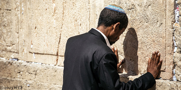 Man in a suit and kippah praying at the Western Wall.