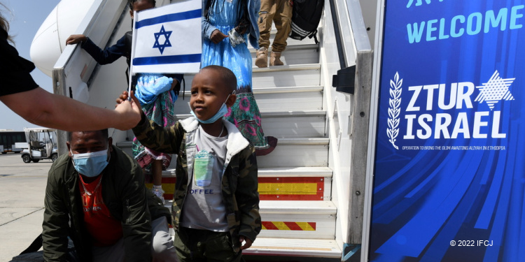 IFCJ volunteer handing a young boy an Israeli flag who just made aliyah.