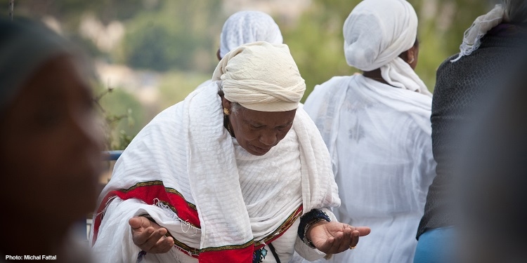 Ethiopian woman wearing white shawl, hand held out as she prays.