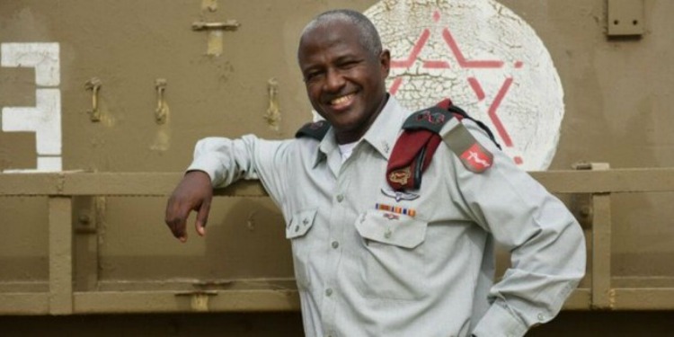 Smiling Ethiopian IDF Colonel leaning up against a tan railing.