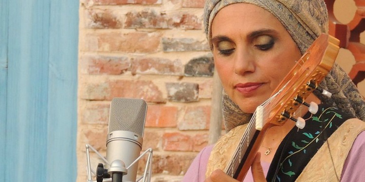 A woman playing a guitar as she has a mic in front of her.