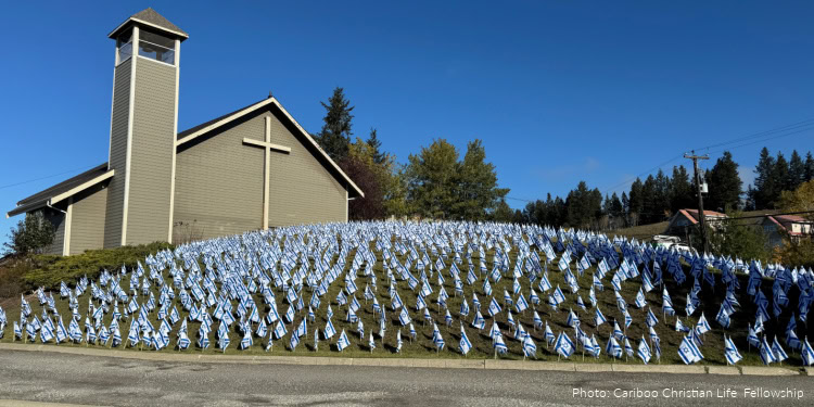 A church building with a cross on the front, surrounded by a large field of blue and white flags, under a clear blue sky.