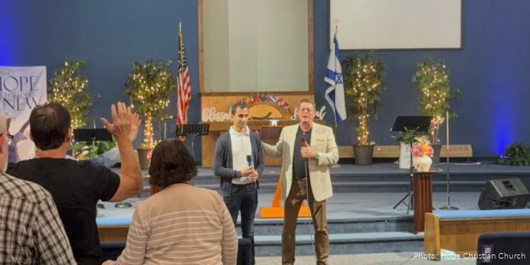 People participating in a fellowship event with flags and stage decorations, including American and Israeli flags, in a church setting.