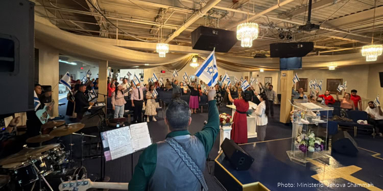 Group of people participating in a fellowship event, waving flags and singing, with musical instruments and stage in the background, celebrating community and faith.
