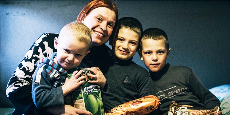 A mother and her three boys, all recipients of IFCJ's program sitting on a bed smiling.