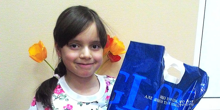 Anya, young IFCJ recipient with fake flowers behind her as she's holding a blue bag.