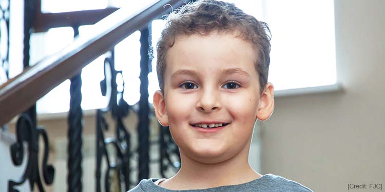 Young boy smiling straight ahead as he's standing on a staircase.
