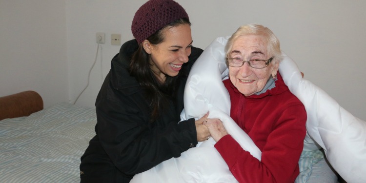 Yael Eckstein sitting with Sarah, an IFCJ recipient on a bed.