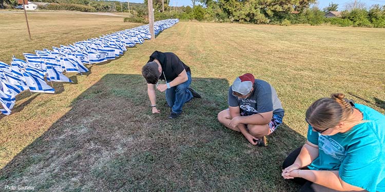 People praying sitting on the grass lined with Israeli flags.