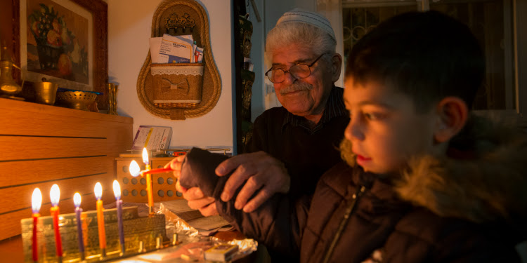 Young boy and an elderly Jewish man lighting a menorah together.