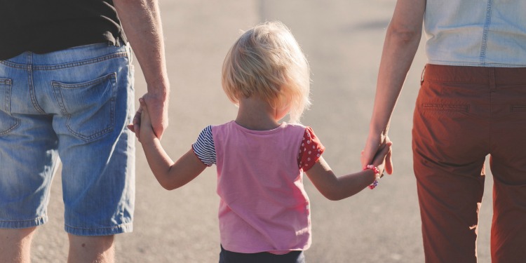 Young blonde girl holding hands with both of her parents