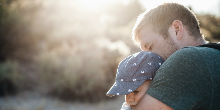 Father hugging his young child while they sit outside.