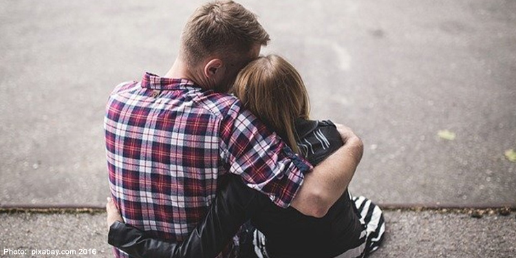 Father and daughter hugging while sitting on the sidewalk.