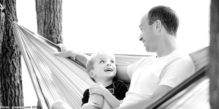 Black and white photo of a father and son sitting on a hammock.