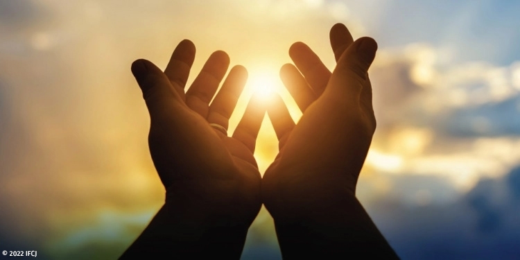 Partially open hands against a sunset background.