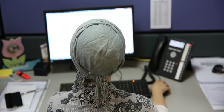 The back view of a person on the computer with a phone next to them.