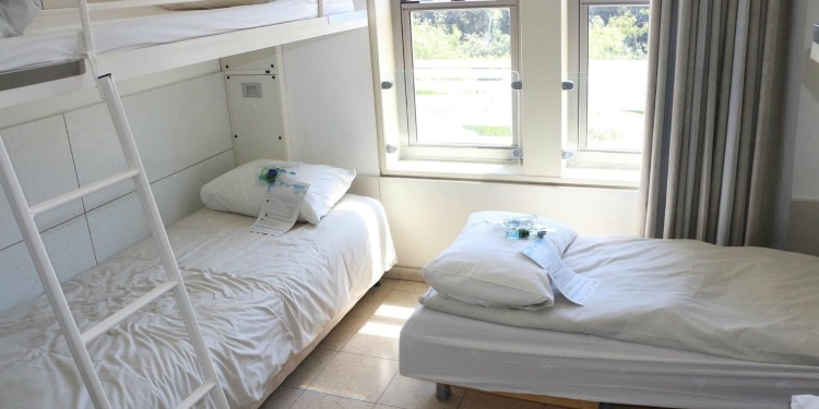 A bunkbed and a single bed all with white sheets and a blue welcome note on it.