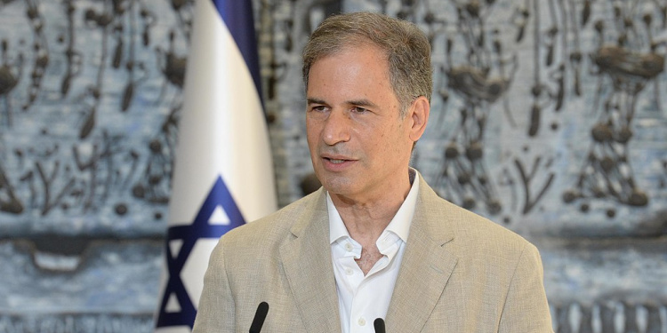 A man giving a speech to a crowd while an Israeli flag is behind him.