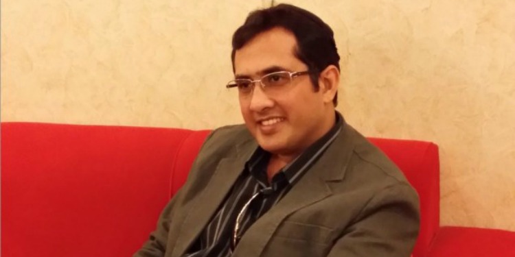 Man with glasses on smiling as he's sitting on a red couch.