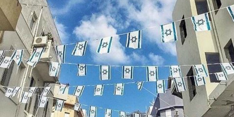 Several rows of small Israeli flags hanging between two buildings.