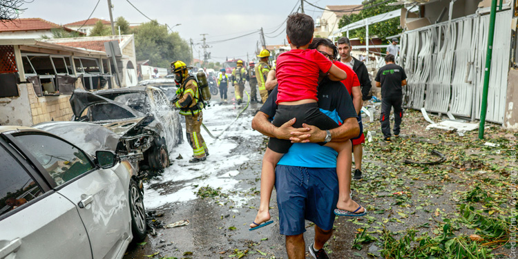 A dad carrying his child while firefighters work to clean up the rocket aftermath in Israel.