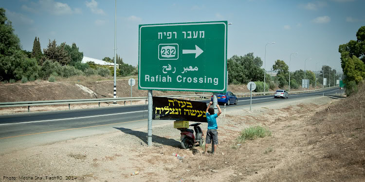 Israelis seen hanging a poster that says "We shall win in God's Will" on a sign pointing to Rafah Crossing near the border with Gaza in Southern Israel on July 20, 2014, during Israel's Operation Protective Edge.