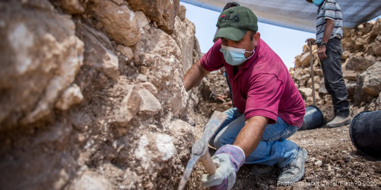 Archaeologist in Central Israel excavating ancient ruins of a 1,300-year-old complex with tools and protective gear.