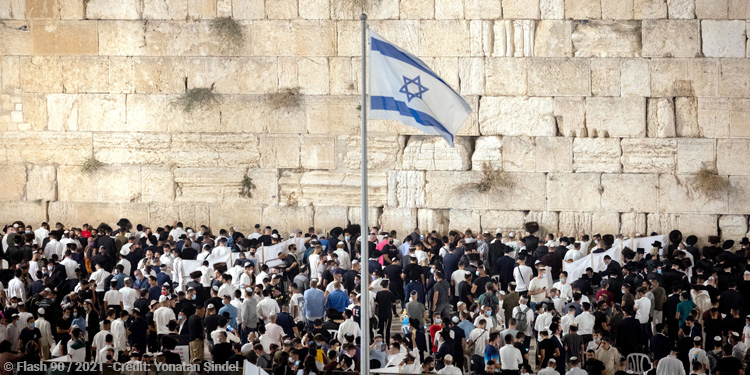 Large crowd of people outside of the Western Wall with the Israeli flag waving.