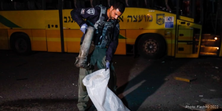IDF soldier inspecting a gas cylinder near a yellow bus at night, wearing tactical gear and gloves, in a security operation in Gaza.