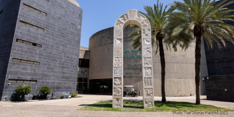 Photograph of a modern museum entrance with a mosaic archway, palm trees, and contemporary architecture, highlighting archaeological and cultural heritage.