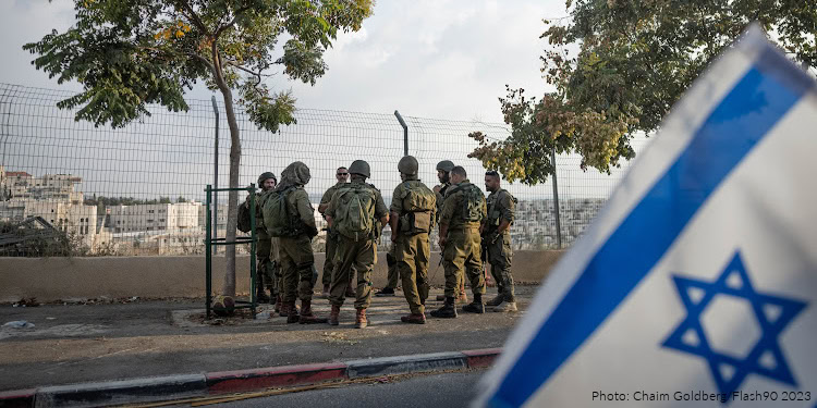 Israeli soldiers standing near a fence with a Gaza flag in the foreground, during a military operation.