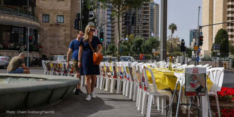 People walk next to a seder table with pictures of Israelis held hostage by Hamas terrorists in the Gaza Strip, on the Eve of the jewish holiday of Passover, in Jerusalem, April 22, 2024.