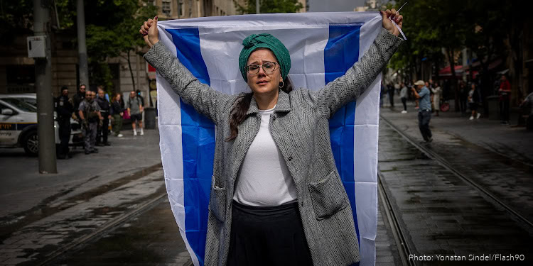 Woman holding Israeli flag during Yom HaShoah remembrance event in a city street, symbolizing unity and resilience in honoring Holocaust victims.