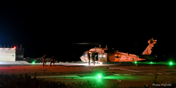 Helicopter rescue operation at night with crew members on the runway, illuminated by green safety lights, highlighting emergency preparedness and aid efforts.