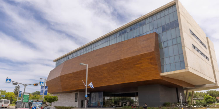 Modern Tel Aviv University research building with unique architectural design and glass facade, under a partly cloudy sky.