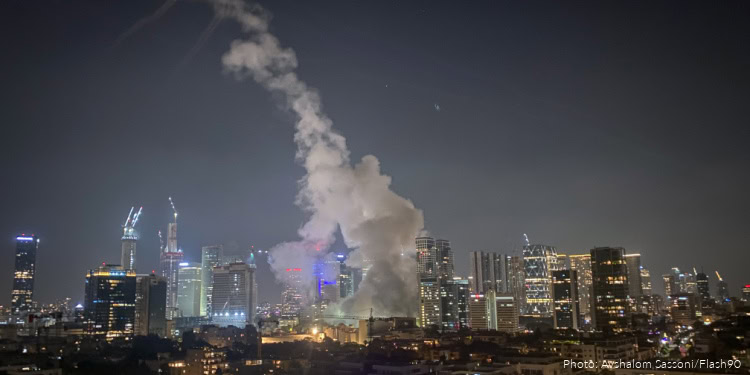 Night cityscape featuring tall buildings, bright lights, and a prominent smoke plume indicating urban emergency or industrial activity.
