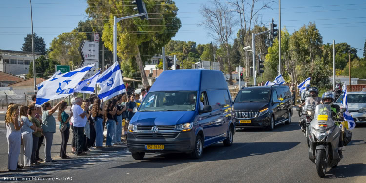 People wave the Israeli flag at the Yad Mordechai junction as they await the funeral procession of slain Israeli hostage Yossi Sharabi, on October 27, 2025.