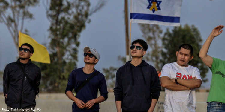 People attend a flag-raising ceremony at the Ma’on Junction on Route 232 in the Eshkol Regional Council, honoring the slain hostages whose bodies were returned over the past week, November 12, 2025. Families of slain hostages removed the photos of those who had been returned and hung a new banner calling for the return of all remaining hostages