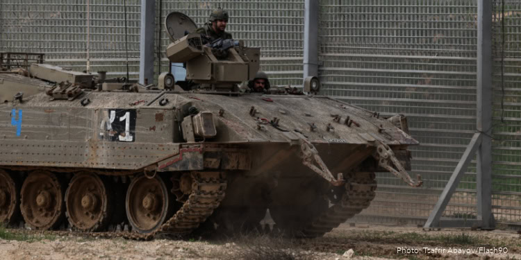 Israeli soldier in a tank driving near the border fence.