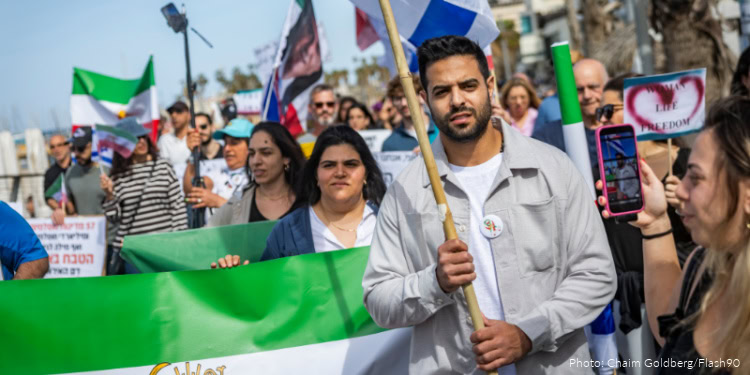 Group of diverse people participating in a community rally, holding flags and banners, promoting support and unity among Jewish communities.