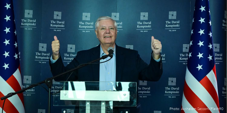 A man speaking at a podium with American flags and a backdrop featuring The David Kempski Institute, celebrating the legacy of Lindsey Graham.