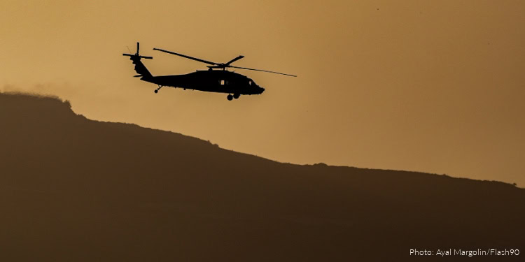 Helicopter performing a rescue operation during sunset, flying over a mountainous area, highlighting emergency aid and humanitarian assistance efforts.