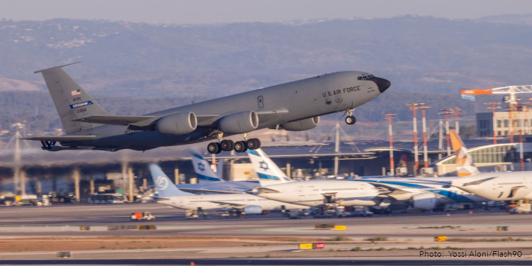 U.S. Air Force C-17 Globemaster III aircraft taking off from an airport runway with other planes and airport infrastructure in the background.