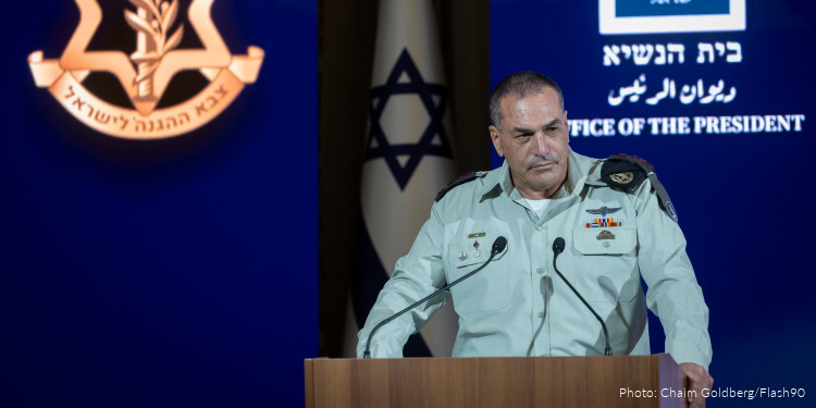 IDF officer speaking at a West Bank event with Israeli flag and government logo in background.