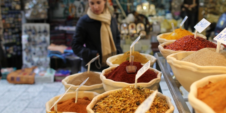 Nine baskets of spices in tan bowls all labeled in a market.