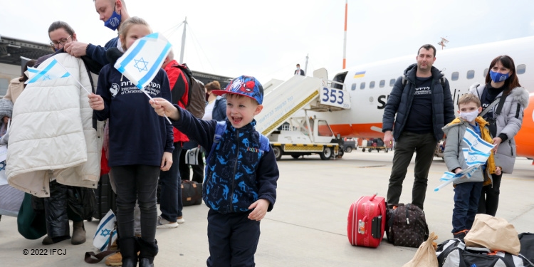 A young boy who just got off an Aliyah flight, among other families waving an Israeli flag.