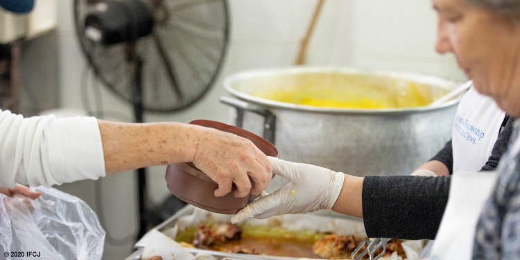 IFCJ staff member handing an elderly Jewish woman a bowl of soup.